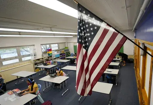 An American flag hangs in a classroom as students work on laptops in Newlon Elementary School, Aug. 25, 2020, in Denver. (AP Photo/David Zalubowski, File)