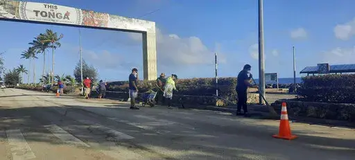 In this photo provided by Broadcom Broadcasting, people clear debris off the street in Nuku’alofa, Tonga, Thursday, Jan. 20, 2022, following Saturday's volcanic eruption near the Pacific archipelago. The first flight carrying fresh water and other aid to Tonga was finally able to leave Thursday after the Pacific nation's main airport runway was cleared of ash left by the eruption. (Marian Kupu/Broadcom Broadcasting via AP)