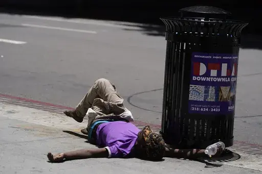 A homeless person lies on the sidewalk while holding a water bottle, Sunday, July 2, 2023, in downtown Los Angeles. Excessive heat warnings remain in place in many areas across the U.S. and are expected to last at least through Monday. (AP Photo/Damian Dovarganes)