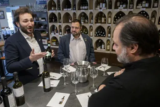 Giorgi Iukuridze, owner and CEO Shabo, a Ukrainian winery, left, and Sam Lerman, CEO of SPYRT Worldwide, introduce Ukrainian wine to the owner of Wine Styles Arthur Lampros, right, at Wine Styles, Dec. 20, 2024 in Dumfries, Va. (AP Photo/Kevin Wolf)