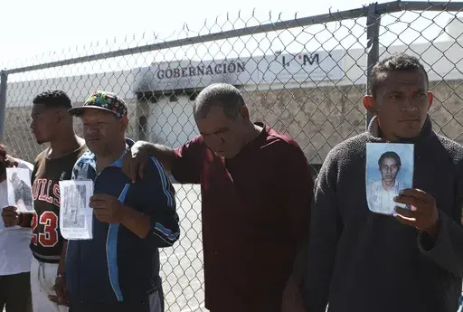 Migrants, mostly from Venezuela, hold photos of those who died in a fire at a Mexican immigration detention center, behind, during a prayer vigil outside the center in Ciudad Juarez, Mexico, April, 27, 2023. Four months after a fire in a Mexican immigration detention center at the border killed 40 migrants, some survivors are living in limbo at a Mexico City hotel, recovering from their injuries and awaiting the prosecution of their captors. (AP Photo/Christian Chavez, File)
