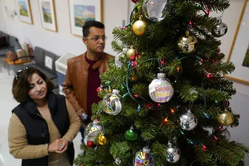 Mohammad Attaie and his wife Deena, newly arrived from Afghanistan, look over ornaments on a Christmas Tree at the Valley Health Center TB/Refugee Program in San Jose, Calif., on Dec. 9, 2021. The staff of Silicon Valley's decades-old refugee health clinic may not all speak the language of the Afghan refugees starting new lives in the San Francisco Bay Area. But they know the anxiety and stress of newcomers who fled war and chaos to end up in a country where they don't speak the language and eve