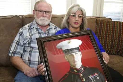 Joey and Paula Reed pose for a photo with a portrait of their son Marine veteran and Russian prisoner Trevor Reed at their home in Fort Worth, Texas, Tuesday, Feb. 15, 2022. Russia is holding Trevor Reed, who was sentenced to nine years on charges he assaulted a police officer. (AP Photo/LM Otero)