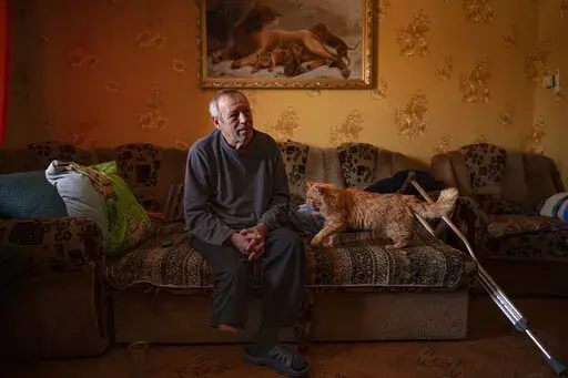 Land mine victim Oleksandr Rabenko, 66 years-old, speaks during an interview with the Associated Press as Murzik, his cat, approaches, at his son's home on the outskirts of Izium, Ukraine, Sunday, Feb. 19, 2023. In this war-scarred city in Ukraine's northeast, residents scrutinize every step for land mines. The brutality of the Russian invasion in this one-time strategic supply hub for Russian troops counts among the most horrific of the war, which entered its second year last month. (AP Photo/V