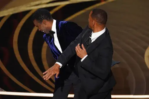 Will Smith, right, hits presenter Chris Rock on stage while presenting the award for best documentary feature at the Oscars on Sunday, March 27, 2022, at the Dolby Theatre in Los Angeles.  On Friday, April 1, The Associated Press reported on stories circulating online incorrectly claiming a photo shows Rock wearing a pad on his cheek during the incident at the Oscars where Smith slapped him. (AP Photo/Chris Pizzello, File)