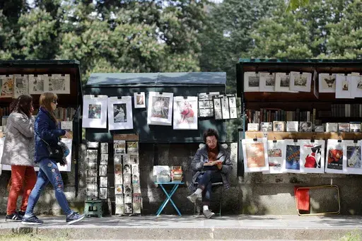 Visitors walk past a bookseller of used and antiquarian books called "Bouquiniste", in Paris, Thursday, May 10, 2018. French President Emmanuel Macron has revealed his bookish side and abandoned plans Tuesday, Feb. 13, 2024, to move the famed second-hand bookseller boxes flanking the banks of the Seine that are beloved by tourists, in preparation for July's Olympics opening ceremony in Paris. (AP Photo/Christophe Ena, File)
