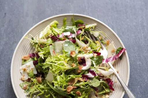 This image released by Milk Street shows a recipe for greens with walnuts, parmesan and pancetta vin. (Milk Street via AP)