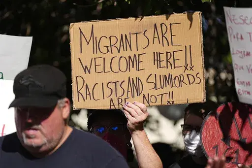 A person holds up a placard during a rally by the East Colfax Community Collective to address chronic problems in the apartment buildings occupied by people displaced from their home countries in central and South America, Sept. 3, 2024, in Aurora, Colo. (AP Photo/David Zalubowski, File)