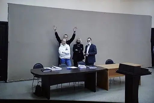 In this image provided by the Russian Federal Penitentiary Service, Russian opposition leader Alexei Navalny waves to journalists and supporters via a video link, as he stands next to his wife Yulia and his layers during a court session in Pokrov, Vladimir region, about 100 kilometers (62 miles) east of Moscow, Russia, Monday, Jan. 17, 2022. A new trial against Russian opposition leader Alexei Navalny has opened at the penal colony where he already is serving a prison term. Navalny is charged wi