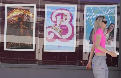 A woman walks past advertisements for the films "Oppenheimer," from left, and "Barbie," on Thursday, July 20, 2023, at the Landmark Theater in Los Angeles. (AP Photo/Chris Pizzello)