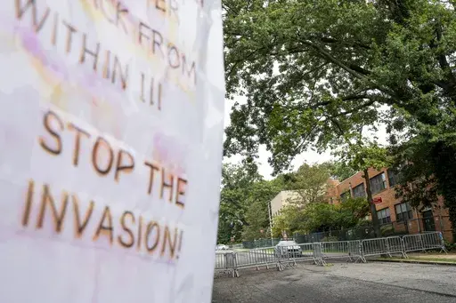 Protest signs are posted outside the former Saint John Villa Academy being repurposed as a shelter for homeless migrants, Wednesday, Sept. 13, 2023, in the Staten Island borough of New York. Scott Herkert, a New Yorker upset that the city has been housing homeless migrants on his suburban block, has set up a loudspeaker to deliver an unwelcoming message in six languages to his new neighbors: "The community wants you to go back to New York City. Immigrants are not safe here." (AP Photo/John Minch