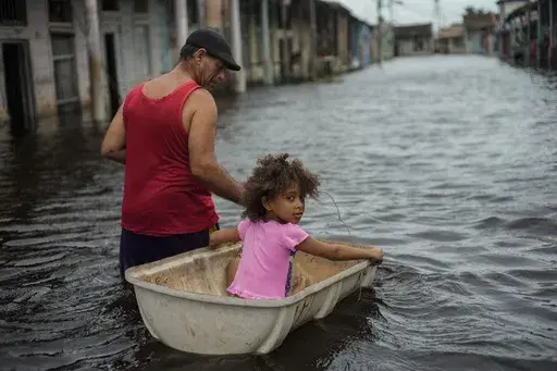 Jesus Hernandez guides his granddaughter Angelina via a container through a street flooded in the passing of Hurricane Helene, in Batabano, Mayabeque province, Cuba, Sept. 26, 2024. (AP Photo/Ramon Espinosa, File)