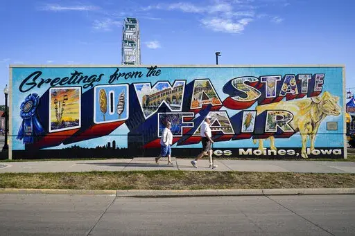 Fairgoers walk past a mural at the Iowa State Fair, Friday, Aug. 19, 2022, in Des Moines, Iowa. Potential White House hopefuls from both parties often swing by Iowa's legendary state fair during a midterm election year to connect with voters who could sway the nomination process. But this year, the traffic at the fair was noticeably light. Democrats are uncertain about President Joe Biden's political future and many Republicans avoid taking on former President Donald Trump. (AP Photo/Charlie Nei