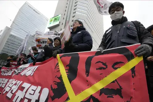 Protesters hold a banner showing images of impeached President Yoon Suk Yeol, right, and acting President Han Duck-soo during a rally demanding the arrest of Yoon in Seoul, South Korea, Saturday, Dec. 21, 2024. The banner reads "Denounce Han Duck-soo's veto." (AP Photo/Ahn Young-joon)
