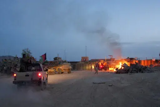 An Afghan National Army pickup truck passes parked U.S. armored military vehicles, as smoke rises from a fire in a trash burn pit at Forward Operating Base Caferetta Nawzad, Helmand province south of Kabul, Afghanistan, April 28, 2011. The Senate is expected to approve on Thursday a large expansion of health care and disability benefits for veterans of Iraq and Afghanistan in response to concerns about their exposure to toxic burn pits.  (AP Photo/Simon Klingert, File)
