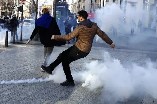 A demonstrator kicks in a tear gas grenade during a protest on the Champs-Elysees avenue, Saturday, Feb.12, 2022 in Paris. Paris police intercepted at least 500 vehicles attempting to enter the French capital in defiance of a police order to take part in protests against virus restrictions inspired by the Canada's horn-honking "Freedom Convoy." . (AP Photo/Adrienne Surprenant)