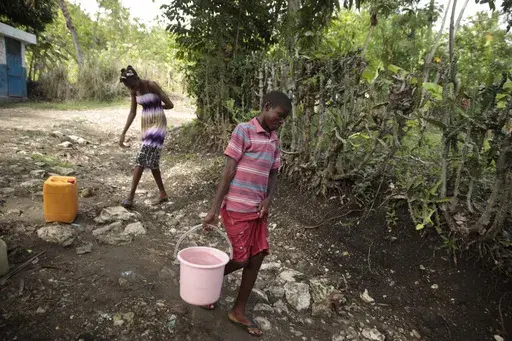 Siblings Mylouise Veillard, left, and Myson walk home with water they collected from a well, for cooking, cleaning and drinking, in a rural area of Saint-Louis-du-Sud, Haiti, Thursday, May 25, 2023. The siblings were considered “poverty orphans" for three years until they were reunited with their mother, Renèse Estève, who had dropped them off at an orphanage where she believed they'd get better care. Their mother brought them home after she was startled at the weight they had lost, convince