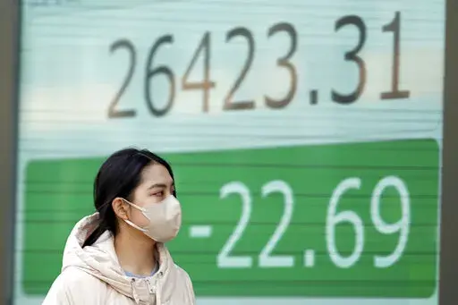 A person wearing a protective mask walks in front of an electronic stock board showing Japan's Nikkei 225 index at a securities firm Thursday, Jan. 12, 2023, in Tokyo. Asian shares were mixed Thursday ahead of a closely watched report on U.S. inflation viewed as a good indicator of whether Wall Street’s recent rising optimism is warranted or overdone. (AP Photo/Eugene Hoshiko)