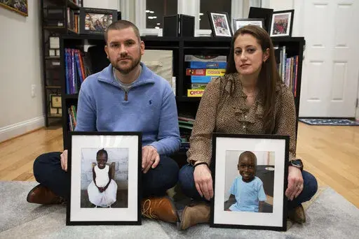 Bryan and Julie Hanlon hold photos of their adopted Haitian children, Gina, left, and Peterson, in a play area of their home in Washington, Tuesday, Feb. 7, 2023. They became the legal parents of the siblings in 2022 and fear they won't be able to secure their passports and fly them out of Haiti. (AP Photo/Cliff Owen)