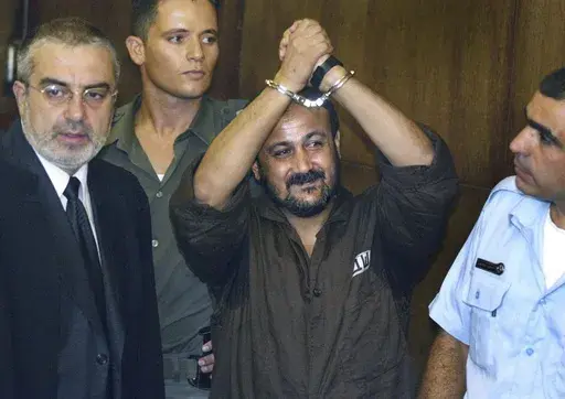Marwan Barghouti, center, raises his handcuffed hands in the air on the opening day of his trial at Tel Aviv's District Court on Aug. 14, 2002. Hamas officials say that any cease-fire deal with Israel should include the release of prisoner Marwan Barghouti — a leader of the militant group's main political rival. The demand by Hamas marks the central role Barghouti plays in Palestinian politics — even after more than two decades behind bars and sentenced by Israel to multiple life terms in pr