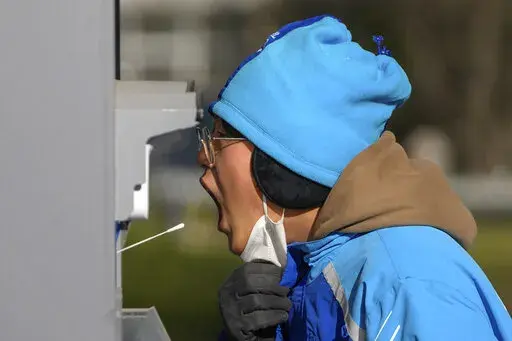A woman has her routine COVID-19 throat swab at a testing site despite authorities starting to ease some of the anti-virus controls in Beijing, Thursday, Dec. 8, 2022. China is the last major country still trying to stamp out transmission of the virus while many nations switch to trying to live with it. As they lift restrictions, Chinese officials have also shifted to talking about the virus as less threatening — a possible effort to prepare people for a similar switch. (AP Photo/Andy Wong)