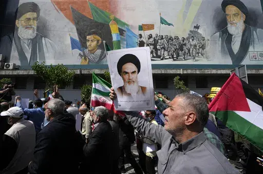 Iranian worshippers walk past a mural showing the late revolutionary founder Ayatollah Khomeini, right, Supreme Leader Ayatollah Ali Khamenei, left, and Basij paramilitary force, as they hold posters of Ayatollah Khomeini and Iranian and Palestinian flags in an anti-Israeli gathering after Friday prayers in Tehran, Iran, April 19, 2024. This month's unprecedented direct attacks between Iran and Israel are revealing deeper insights into both militaries. Experts say Friday's apparent precision str