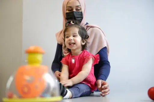 In this photo provided by the Children's Hospital of Eastern Ontario, Ayla Bashir sits with her mother, Sobia Qureshi, during a physical therapy assessment for Ayla at CHEO in Ottawa on Aug. 23, 2022. The toddler is the first child treated as fetus for Pompe disease, an inherited and fatal disorder in which the body fails to make some or all of a crucial protein. (André Coutu/CHEO via AP)